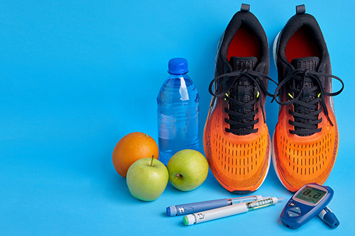 Orange running shoes, blue water bottle, two green apples, an orange and diabetic supplies on a blue background